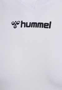 Maglia sportiva bianca con tessuto testurizzato, dotata di un logo nero e del nome del marchio "hummel" sul lato sinistro in alto. Design a V.