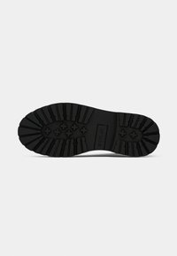 Semelle de chaussure en caoutchouc noir avec des crampons profonds et des motifs en croix, arborant le logo de la marque "REPLAY" près du centre.