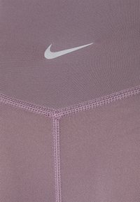 Tissu de sport violet avec une texture lisse, présentant un logo Nike blanc en contraste. Comprend des coutures surpiquées pour plus de détails.