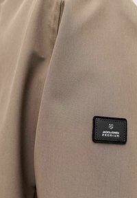Tissu beige avec un gros plan sur un patch rectangulaire noir étiqueté "JACK & JONES PREMIUM" cousu sur le matériau.