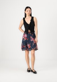 Fekete fodros crop top V-nyakkal, kék virágmintás A-vonalú szoknyával kombinálva, amely színes virágmintákat tartalmaz. A megjelenést fekete lapos cipők teszik teljessé.