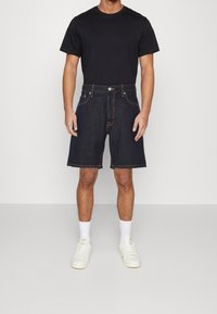 Jeansshorts i mörkblått med en avslappnad passform, med kontrasterande sömmar, fem fickor och knappstängning. Matchas med en svart t-shirt och vita sneakers.