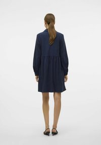 Marine jurk met lange mouwen, een getailleerde bovenkant en een gerimpelde taille. Soepele textuur en een knielange snit. Achteraanzicht met een kraag.