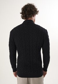Getextureerde zwarte gebreide sweater met een kabelpatroon, lange mouwen en een geribde kraag en manchetten, weergegeven vanuit de achterkant.