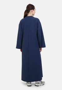 Dlouhé oversize šaty navy modré barvy s vysokým výstřihem, spadlými rameny a širokými rukávy; hladká, měkká textura; jednoduchý detail zadního švu.