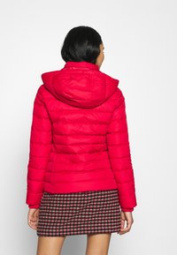 Czerwona kurtka puchowa z kapturem, z pikowanym wzorem, długimi rękawami i dopasowanym krojem, zestawiona z kraciastą spódnicą.