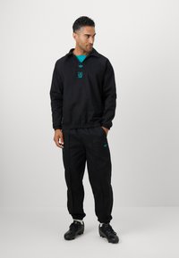 Zwart sportoutfit bestaande uit een sweatshirt met een kraag en een bijpassende joggingsbroek, beide met turquoise logo-accenten.