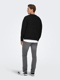 Black knit sweater with a loose fit, gray tapered pants, and black and white sneakers. Textured fabric and simple design.