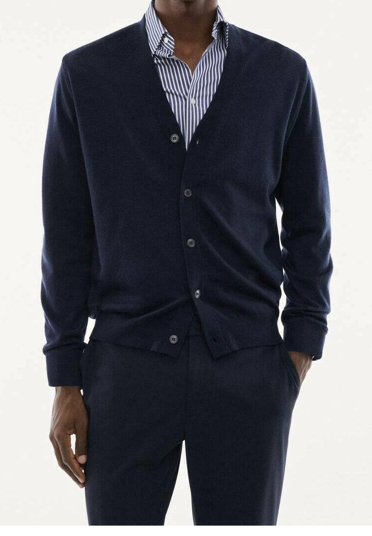 Homme portant un cardigan bleu foncé boutonné sur une chemise rayée bleue et blanche avec col, et un pantalon bleu foncé assorti. Mains dans les poches.