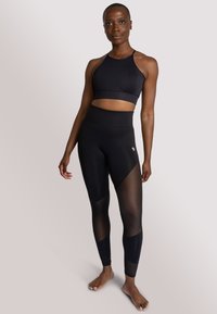 Reggiseno sportivo nero e leggings neri a vita alta con pannelli in rete trasparente. Il tessuto è liscio e con una vestibilità aderente, che mette in evidenza i contorni del corpo.
