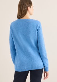 Hellblauer Pullover mit weicher Textur, rundem Ausschnitt und geripptem Saum sowie Bündchen. Lange Ärmel, lockere Passform, sichtbare Nahtdetails.