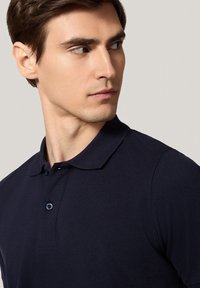 Granatowa koszulka polo z krótkim rękawem, wykonana z teksturowanej tkaniny, z klasycznym kołnierzykiem i zapięciem na dwa guziki.