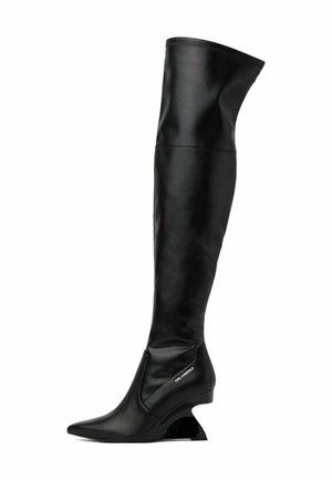 Botte haute en cuir noir à talon haut avec bout pointu et talon sculpté courbé, avec un petit logo près de la cheville.