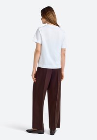 T-shirt bianco a maniche corte con una vestibilità rilassata, abbinato a pantaloni larghi marroni e scarpe basse marroni. Collo semplice, texture del tessuto liscia.