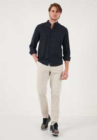 Camisa azul marino de botones con cuello mao, combinada con pantalones beige y zapatillas negras con acentos grises. Tela suave, ajuste casual.