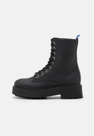Stivaletto nero con lacci, suola spessa, finitura in pelle liscia, occhiali argentati e un accento blu sul tallone.