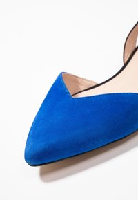 Blaue Wildleder-Pumps mit spitz zulaufender Zehenpartie und einem Cut-out-Design an den Seiten, ausgestattet mit einem glatten Innenfutter und einer schwarzen Sohle.