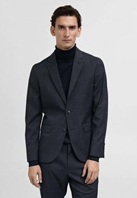 Dark gray tailored blazer with a subtle check pattern, single button closure, notched lapels, and two front pockets. Worn over a black turtleneck.