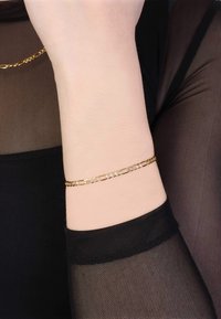 Gold chain bracelet with rectangular links and small clear stones. Worn on a wrist, paired with a black sheer top.