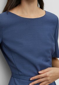 Robe à carreaux bleus avec un col bateau, des manches courtes et une taille cintrée. Le tissu semble texturé et doux.