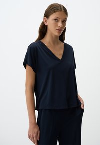 T-shirt blu navy a V con maniche corte, vestibilità rilassata, tessuto morbido, senza motivi o dettagli visibili, abbinato a pantaloni coordinati.