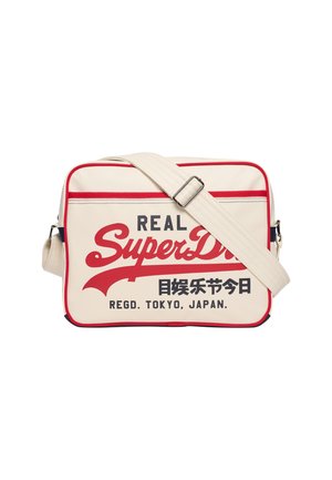 Sac d'épaule rectangulaire crème avec bordure rouge, sangle réglable et logo "Real SuperDry" avec des caractères japonais et le texte "Regd. Tokyo, Japan".