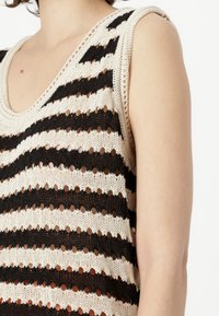 Πλεκτό τοπ με χαλαρή εφαρμογή, με εναλλασσόμενες φαρδιές μαύρες και κρεμ ρίγες, και ύφασμα ανοιχτής ύφανσης.