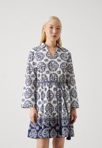 Rochie albă cu model floral albastru, guler, mâneci tip clopot, cordon la talie și margine etajată cu broderie detaliată la baza.