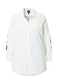 Camicia bianca con bottoni, maniche lunghe, dotata di taschino sul petto e motivo a pois neri sulle maniche. Realizzata in un tessuto leggero.