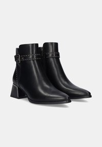Botas de cuero negro hasta el tobillo con puntera puntiaguda, cierre de cremallera, detalle de correa con tachuelas y tacón cuadrado. Textura suave con un diseño elegante.