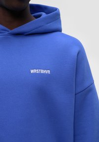 Felpa blu con cappuccio caratterizzata da una texture morbida, vestibilità oversize e la scritta ricamata "WRSTBHR" in bianco sul petto.