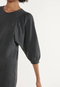 Vestido de pulóver gris oscuro con escote redondo, mangas abullonadas y detalles cosidos a lo largo de las costuras laterales. Tejido suave con un corte relajado.