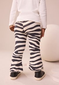 Zebraskrå-printede vidde bukser i creme og mørkegråt ribbet stof med bølget kant, kombineret med sorte sneakers.