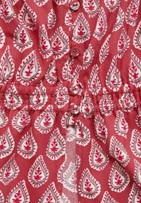 Red patterned fabric features white leaf motifs outlined in dark red, with buttons and a gathered waist detail. Soft texture and lightweight material.