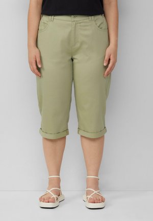 Khaki 7/8 broek met opgerolde pijpen, voorzien van voorzakken en een gladde textuur. Gecombineerd met witte sandalen met bandjes.