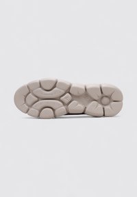 Suela de sneaker color beige claro con una superficie texturizada, que presenta un patrón distintivo de formas circulares y ovaladas para agarre y tracción.
