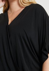 Czarny top z lekkiego materiału z dekoltem w serek, drapowanym fasonem i krótkimi rękawami. Gładka faktura i minimalistyczne detale.
