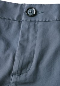 Primo piano di pantaloni in tessuto grigio che presenta un bottone nero lucido, cuciture curate e una texture liscia con minime pieghe.