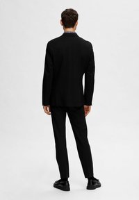 Črn suknjič s prilagojeno zasnovo, zadnji pogled. Ima klasične reverje in subtilne detajle na ovratniku srajce. Teksturovana tkanina in krojen fit.