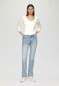 Bílý přiléhavý top s výstřihem do V, doplněný světle modrými zvonovými džíny. Outfit doplňují robustní bílé tenisky.