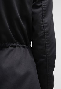 Czarna kurtka z taliowanym pasem z elastycznymi detalami, gładką fakturą tkaniny i eleganckim, dopasowanym krojem.