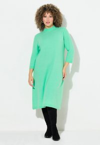 Abito a maglia verde menta con scollo alto, maniche a tre quarti e vestibilità rilassata, abbinato a stivali neri al di sopra del ginocchio.