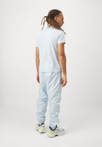 Gai zila polo krekls apvienots ar gaiši ziliem pieguļošiem biksēm. Biksēm ir elastīgas piedurknes un kabatas, ko papildina balta apavi ar akcentiem.