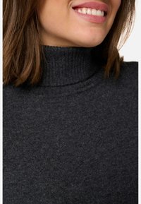Pull en turtleneck tricoté gris avec une texture côtelée et une coupe ajustée, mettant en avant un look classique et polyvalent.