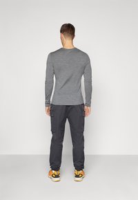 Grå langermet skjorte, slim fit, parret med svarte cargo-bukser med sidelommer og oransje joggesko, sett fra baksiden.