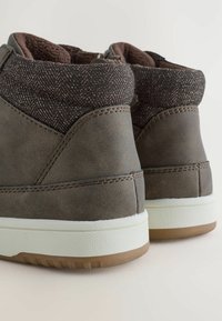 Bruna hög-top sneakers med en texturerad tygkrage, vit mellansula och gummiyttersula. Har sydda detaljer på en slät lärokropp.