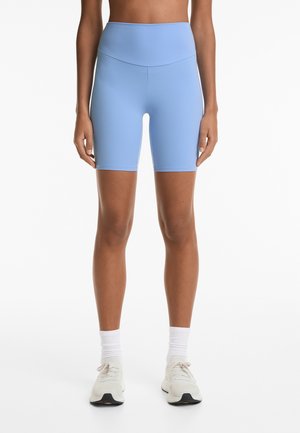 Blauwe high-waisted biker shorts van een soepele stretchstof, ontworpen met een snit tot halverwege de dij, gecombineerd met witte sportschoenen en crew-sokken.