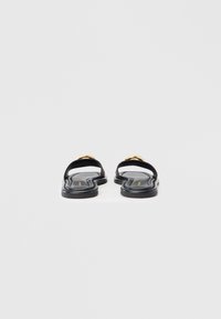 Sorte sandaler med flade såler, med en glat tekstur, åben tå-design og gulddetaljer på stroppen.