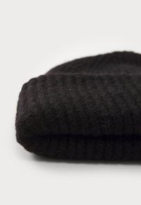 Caciula neagră tricotată cu o textură ribbed, fabricată din lână moale. Are un mansetă pliată și un aspect gros și confortabil.