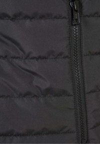 Detail černé vycpané bundy se zipovým uzávěrem a horizontálním prošíváním. Tkanina má hladkou strukturu s matným povrchem.